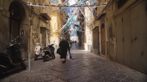 Banderas,-Banderines-Y-Serpentinas-Se-Extendían-Por-La-Calle-De-Nápoles,-Una-Anciana-Caminando-Por-Las-Calles-Estrechas