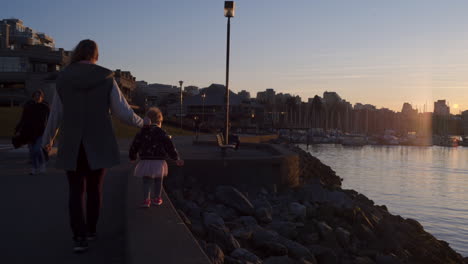 Toma-De-Seguimiento-De-Una-Madre-Y-Su-Hija-Caminando-Por-El-Malecón-Durante-La-Puesta-De-Sol.