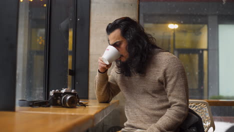 A-Contemplative-Indian-Man-Drinks-Coffee-in-a-Warm-Café-on-a-Cold-Snowy-Day