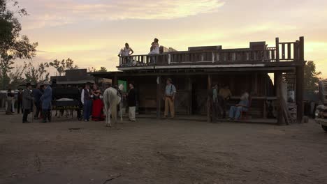 Vintage-period-wild-west-reenactment-scene-in-front-of-saloon-building-with-authentic-cowboy-costume-people-walking-in-scene