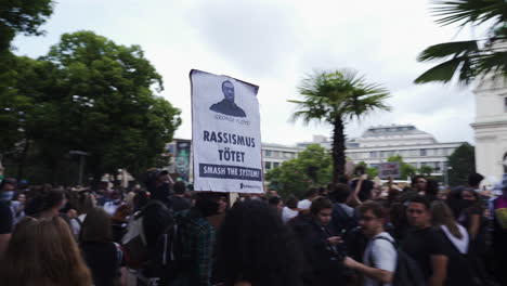 Eine-Folgeaufnahme-Einer-Frau,-Die-Ein-Schild-In-Der-Hand-Hält,-Während-Sie-Durch-Eine-Menschenmenge-Geht-Und-Gegen-Rassismus-Protestiert