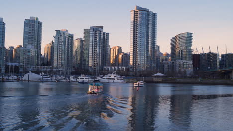 Una-Toma-Amplia-De-Un-Aquabus-Conduciendo-Hacia-El-Muelle-De-Yaletown-Con-La-Puesta-De-Sol-En-El-Centro-De-Vancouver-En-La-Distancia