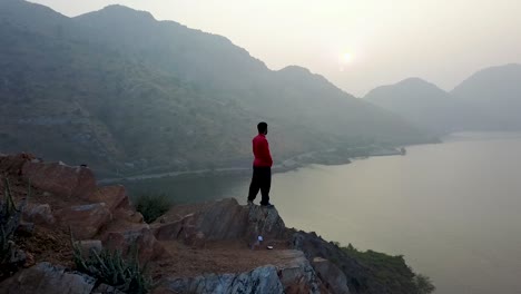 Joven-Parado-En-El-Borde-Del-Acantilado-Junto-Al-Lago-Badi-En-Una-Mañana-Brumosa-En-Udaipur,-Rajasthan,-India