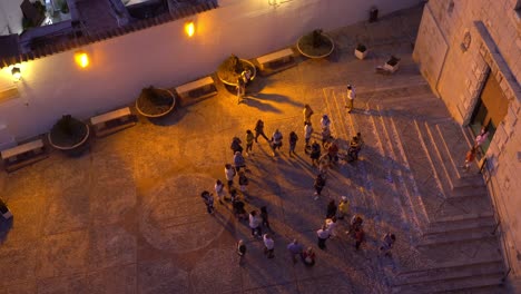 Group-of-people-waiting-in-front-of-a-church-at-dusk-whiile-tourists-walk-in-and-out-shot-from-the-top