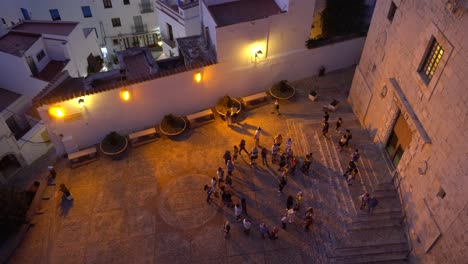 Grupo-De-Personas-Esperando-Frente-A-Una-Iglesia-Al-Atardecer-Mientras-Los-Turistas-Entran-Y-Salen-Disparados-Desde-Arriba-Con-Una-Vista-Amplia