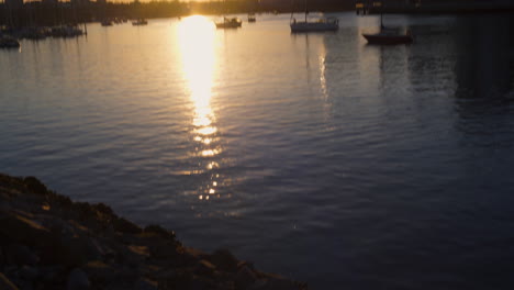 TILTING-UPWARD-SHOT-to-Reveal-Vancouver's-City-Skyline-Illuminated-by-the-Evening-Light,-Boats-Float-in-the-Distance