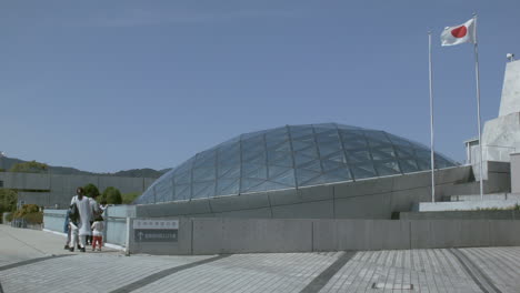 Tourists-admiring-a-glass-dome-building,-with-a-Japanese-flag-flying,-in-Nagasaki,-Japan