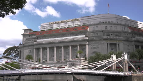 Eine-Zeitrafferaufnahme-Des-Legendären-Fullerton-Hotels-In-Singapur-An-Einem-Sonnigen-Nachmittag-Mit-Klarem-Blauen-Himmel-Und-Der-Cavenagh-Bridge