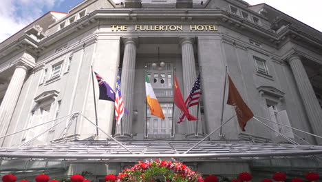 A-still-shot-of-the-top-of-the-main-entrance-lobby-at-The-Fullerton-Hotel-Singapore-wit-flags-blowing-in-the-sea-breeze-in-the-afternoon-clear-blue-sky