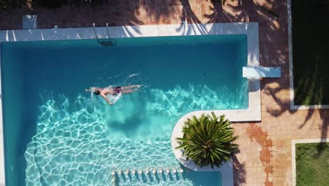 Hombre-Nadando-En-Una-Piscina-De-Lujo:-Vista-Aérea-Ascendente-De-Pájaro