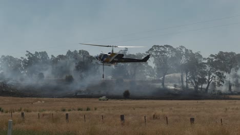 Helicóptero-Acercándose-A-La-Presa-Con-Otros-Bomberos-Al-Fondo-Cerca-Del-Fuego-De-Hierba