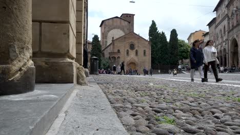 Vista-De-ángulo-Bajo-De-Turistas-Caminando-Por-La-Plaza-Santo-Stefano-Con-La-Basílica-De-Santo-Stefano-Al-Fondo-En-Bolonia