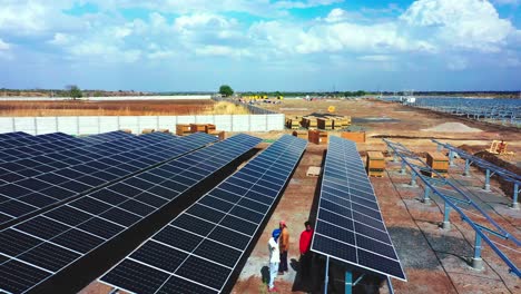 Drone-camera-moving-around-where-solar-panels-and-modules-are-being-fitted-with-cool-landscape-and-agricultural-fields-in-the-background