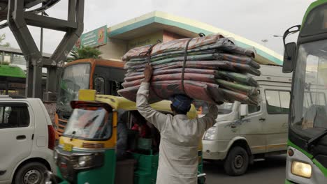 Hombre-Indio-Que-Llevaba-Un-Gran-Bulto-Sobre-Su-Cabeza,-Esperando-Para-Cruzar-La-Calle,-Delhi,-India