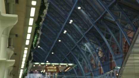 A-commuter-relaxes-while-people-busily-walk-past-him-and-the-camera-tilts-up-to-show-the-architecture-of-the-St-Pancras-International-Station-in-London