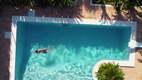 Hombre-Nadando-En-Una-Piscina-De-Lujo:-Vista-Aérea-Ascendente-De-Pájaro