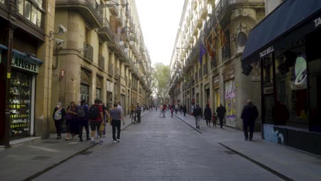 Forward-shot-through-long-central-street-in-Barri-Gothic-quarter-of-Barcelona-with-people-starting-their-day-in-the-morning-and-walking-over-pavement