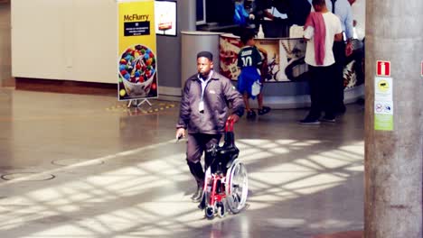 Trabajador-Afroamericano-Negro-Rodando-Silla-De-Ruedas-Plegada-En-El-Aeropuerto,-Cámara-Lenta