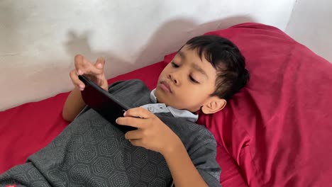 Un-Niño-Asiático-De-4-Años-Jugando-En-Su-Teléfono-Inteligente-Mientras-Está-Acostado-En-La-Cama