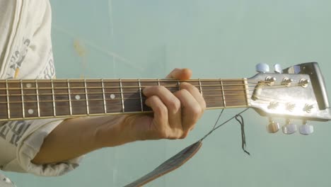 Cerca-De-La-Mano-De-Un-Joven-Tocando-La-Guitarra-Durante-La-Puesta-De-Sol-Junto-Al-Agua-En-El-Puerto-Comercial-De-Barcelona,-España