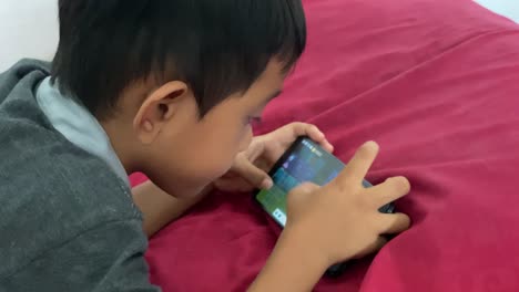 Ein-4-jähriger-Asiatischer-Junge-Spielt-Auf-Seinem-Smartphone,-Während-Er-Im-Bett-Liegt