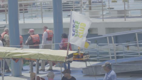 Ein-Boot-Mit-Touristen-Verlässt-Den-Peer,-Während-Eine-Gruppe-Von-Touristen-Mit-Orangefarbener-Schwimmweste-Auf-Die-Panga-Fahrt-Auf-Den-Galapagos-Inseln-Wartet