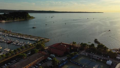 Vista-Aérea-De-Drones-Hacia-Adelante-En-Rápido-Movimiento-De-Portoroz-Con-Barcos-En-El-Mar-A-La-Luz-Amarilla-Del-Atardecer,-Eslovenia