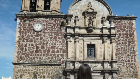 Parroquia-Santiago-Apostol-Hito-Inclinado-Hacia-Abajo-Revelando-Modelo-Morena-Caminando-En-La-Plaza-De-Tequila-En-Jalisco,-México---Cámara-Lenta