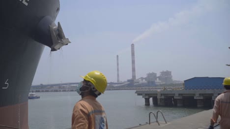 Longshoreman-In-Face-Mask-And-Hard-Hat-Looking-Up-At-Large-Shipping-Vessel-At-The-Port-During-Global-Pandemic