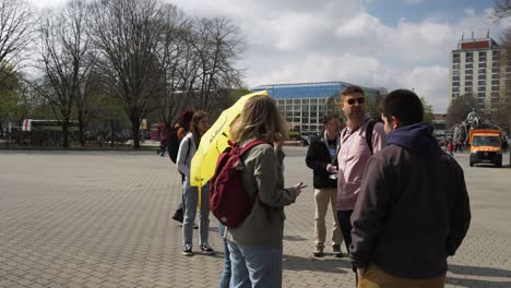 Menschen-Warten-Neben-Einem-Wanderführer-Mit-Gelbem-Regenschirm-In-Berlin-In-Der-Nähe-Des-Neptunbrunnens