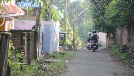 Un-Par-De-Amigos-Andando-En-Motocicleta-Y-Usando-Casco-Con-Sus-Mochilas-Viajando-Por-La-Calle-Angosta-En-Varkala,-India