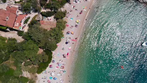 Grúa-Aérea-Bajando-Sobre-Gente-Tomando-El-Sol-En-La-Playa-De-Dubovica,-Isla-De-Hvar,-Croacia