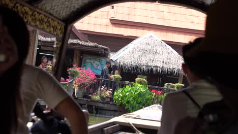 Tourists-in-Boat-Watching-Restaurant-and-Shops-on-Floating-Market-in-Ancient-Siam-Open-Museum,-Thailand