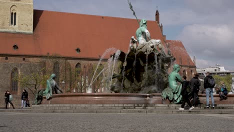 Turistas-Pasando-Por-La-Fuente-De-Neptuno-En-Berlín-Con-La-Iglesia-De-Santa-María-Al-Fondo