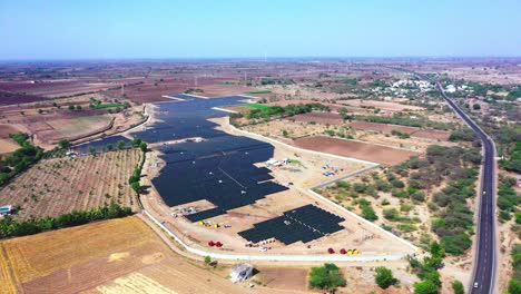 An-aerial-drone-camera-is-rotted-view-of-the-road-and-nearby-agricultural-farms-where-solar-modules-are-used-to-produce-green-energy