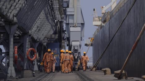 Group-Of-Stevedores-On-The-Platform-Of-Paradip-Port-In-Odisha,-India-With-Large-Equipment-And-Container-Ship-Anchored