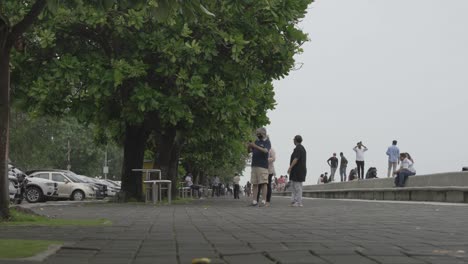 Tourists-Walking-On-The-Promenade-Stops-And-Taking-Pictures-Beside-The-Lush-Green-Trees-In-Mumbai,-India