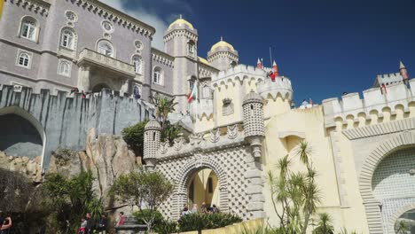 Nach-Oben-Neigende-Zeitlupenaufnahme,-Touristen,-Die-Um-Den-Pena-Nationalpalast-In-Sintra,-Portugal,-Spazieren,-Blauer-Himmel-Im-Hintergrund