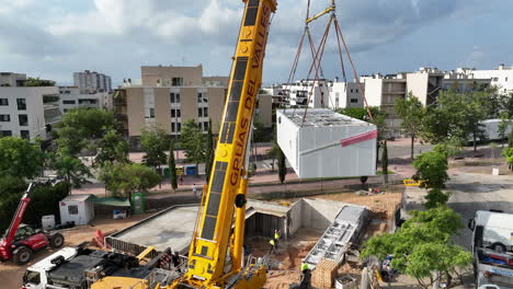 Vista-Aérea-De-Una-Grúa-Circular-Levantando-Un-Proyecto-De-Vivienda-Modular-Inteligente-Sobre-Los-Cimientos-Del-Sitio-De-Construcción.