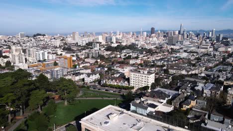 Las-Imágenes-De-Drones-Presentan-Una-Vista-Serena-De-Las-Siete-Damas-Pintadas-De-San-Francisco,-Casas-Victorianas-Icónicas,-En-Contraste-Con-El-Vibrante-Paisaje-Urbano-Y-La-Exuberante-Vegetación-Del-Parque-Alamo-Square.