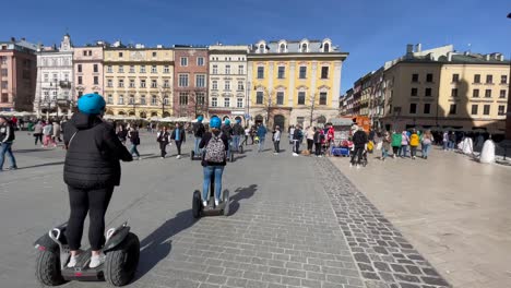 Tourists-sightseeing-with-electronic-scooters-on-the-streets-of-Krakow-main-market-square,-Krakow-Poland-urban-scene