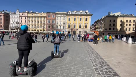 Turistas-Haciendo-Turismo-Con-Scooters-Electrónicos-En-Las-Calles-De-La-Plaza-Principal-Del-Mercado-De-Cracovia,-Escena-Urbana-De-Cracovia,-Polonia