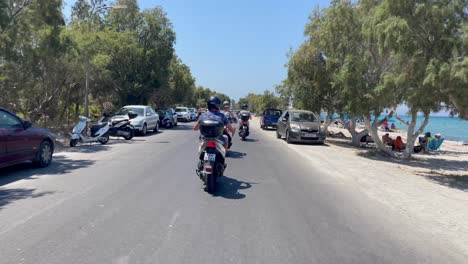 Touristen,-Die-Motorroller-In-Der-Strandstraße-Des-Inseldorfes-Kos-Fahren