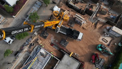 Vista-Aérea-Mirando-Hacia-Abajo-Grúa-De-Construcción-Instalando-Un-Módulo-De-Vivienda-Inteligente-En-Los-Cimientos-Del-Sitio-De-Construcción