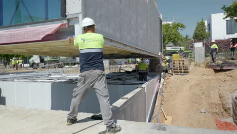 Trabajador-Contratista-De-Construcción-Guiando-La-Unidad-De-Vivienda-Modular-Inteligente-A-Cámara-Lenta-Sobre-Los-Cimientos