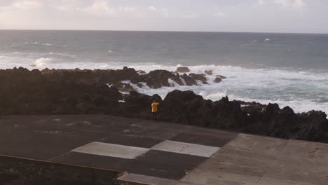 Hombre-Chaqueta-Amarilla-De-Pie-Frente-A-Grandes-Olas-Del-Mar-Agitado,-Azores-Portugal