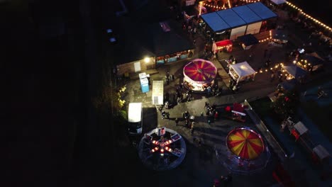 Atracción-De-Feria-Navideña-Iluminada-En-El-Aparcamiento-Del-Barrio-En-La-Vista-Aérea-Nocturna