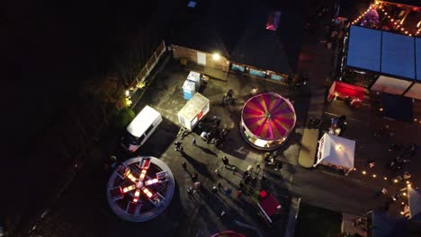 Atracciones-De-Feria-Navideñas-Iluminadas-En-El-Aparcamiento-Del-Pub-Del-Barrio-Por-La-Noche-Vista-Aérea