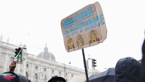 Aufnahme-Eines-Schildes-Mit-Der-Aufschrift-„Weißes-Schweigen-Ist-Compliance“-Und-Affen-Emojis-Während-Einer-Protestaktion-Vor-Einem-Wichtigen-Gebäude-In-Wien,-Österreich