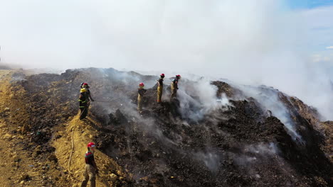 Aerial,-drone-shot-of-Firefighters-extinguish-a-wildfire,-in-middle-of-rising-smoke,-sunny-day,-in-Dominican-Republic